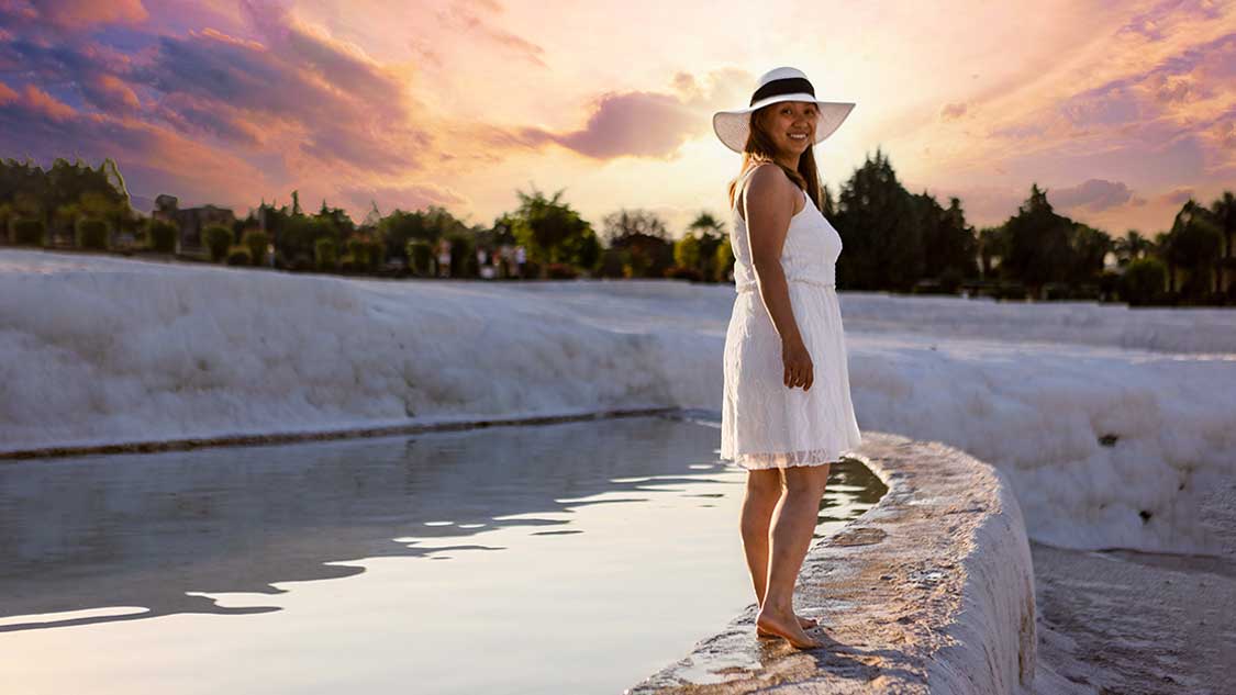 Woman walking along geothermal pools at sunrise in Pumakkale, Turkiye