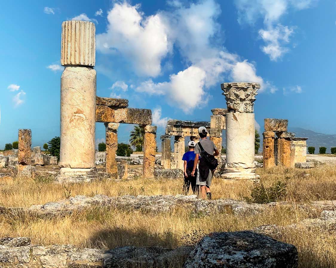 Two boys walk through a field dotted with Roman columns in Heirapolis, Turkiye