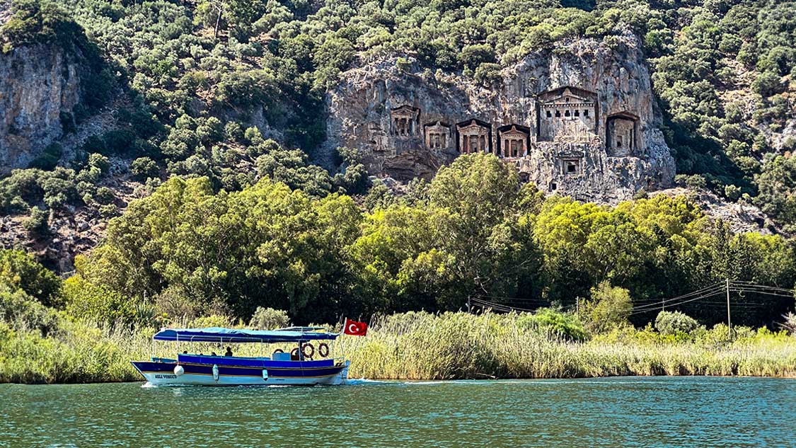 A tour boat cruises past the Lycian tombs in Dalyan, Turkiye