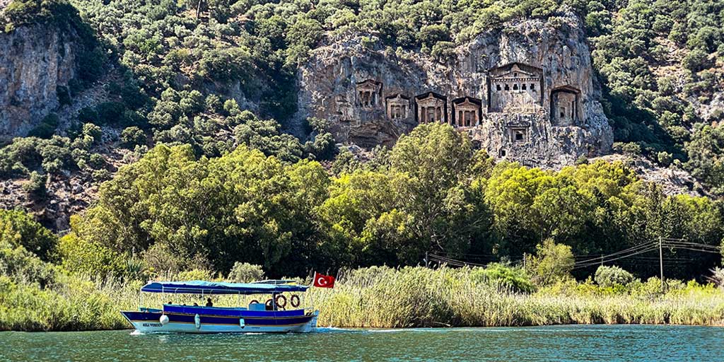 A tour boat cruises past the Lycian tombs in Dalyan, Turkiye