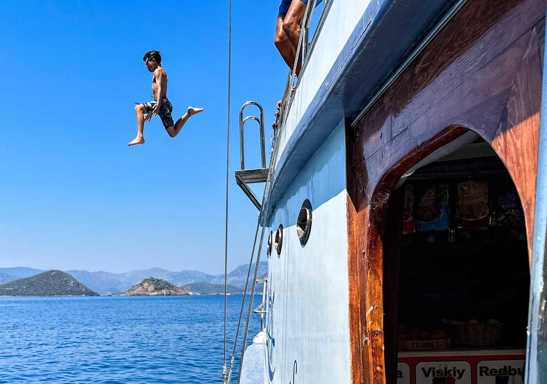 A young boy jumps from the deck of a Gocek boat on a 12 Islands Cruise