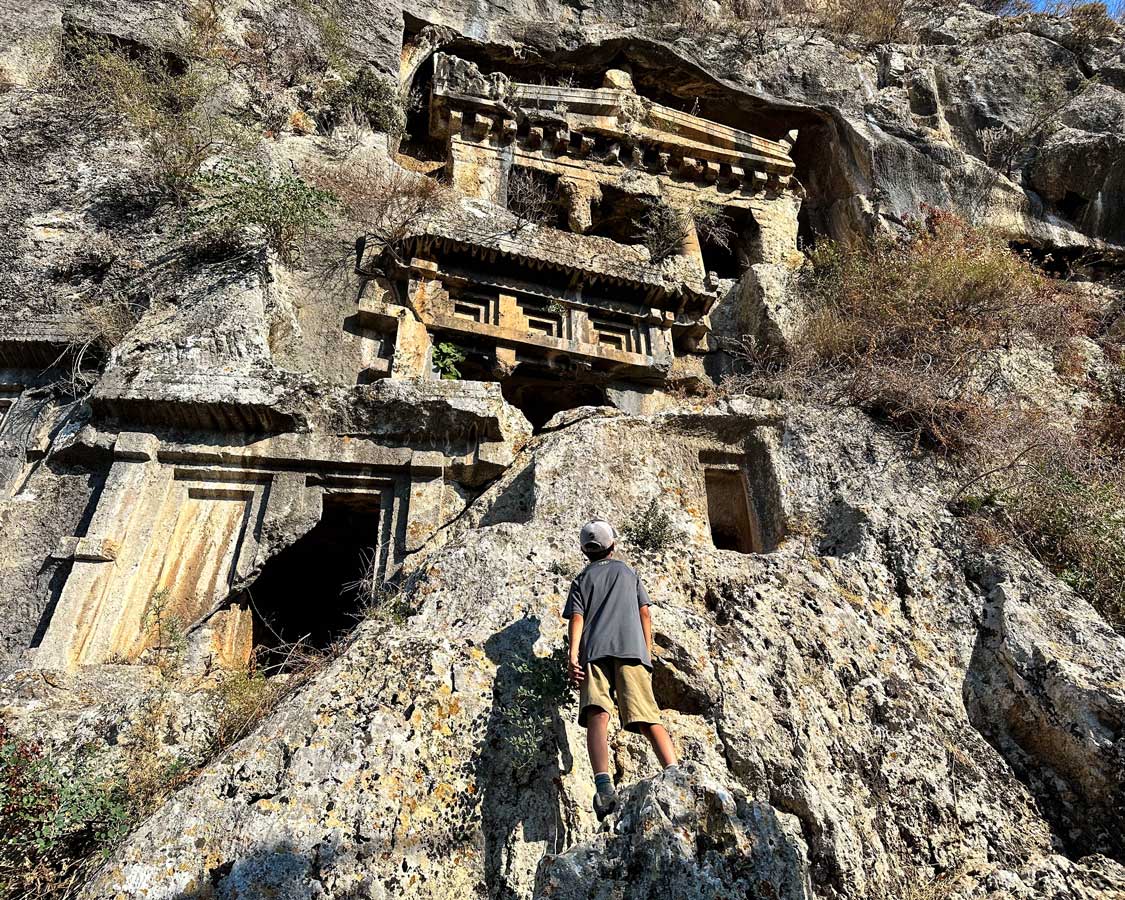 A boy stands on a rock while looking up at ancient Lycian rock tombs in Fethiye