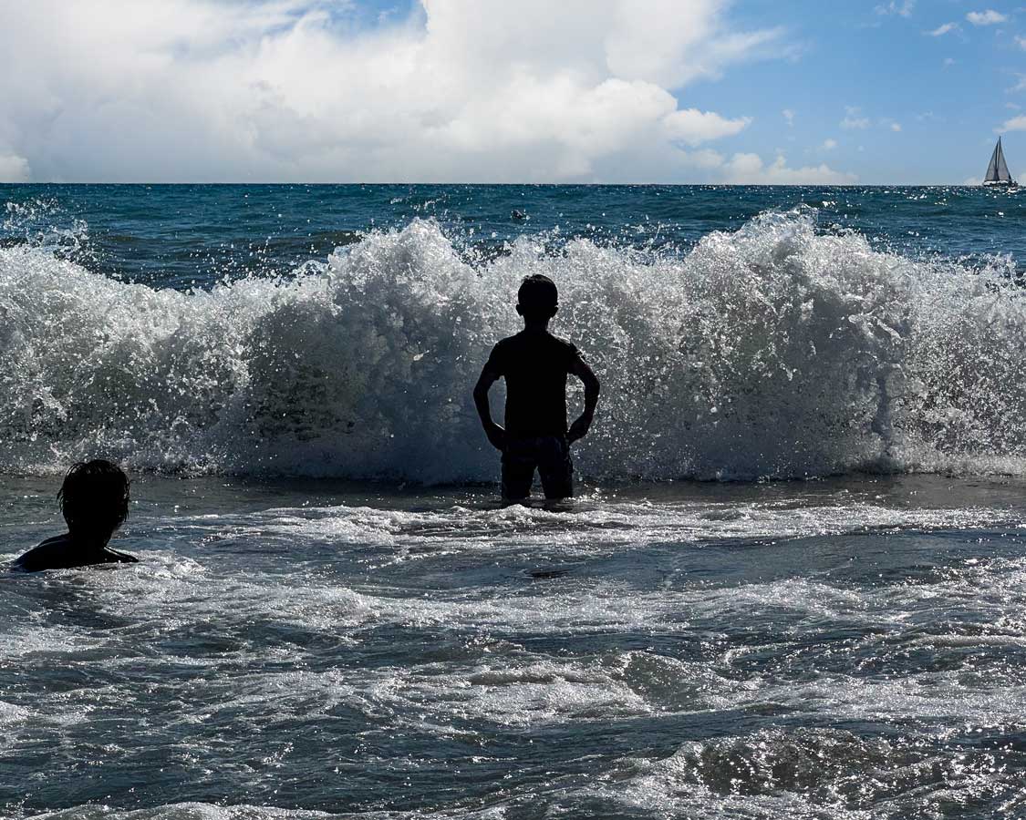 A boy is silhouetted against a large wave in the pounding surf of Patara Beach, Turkiye