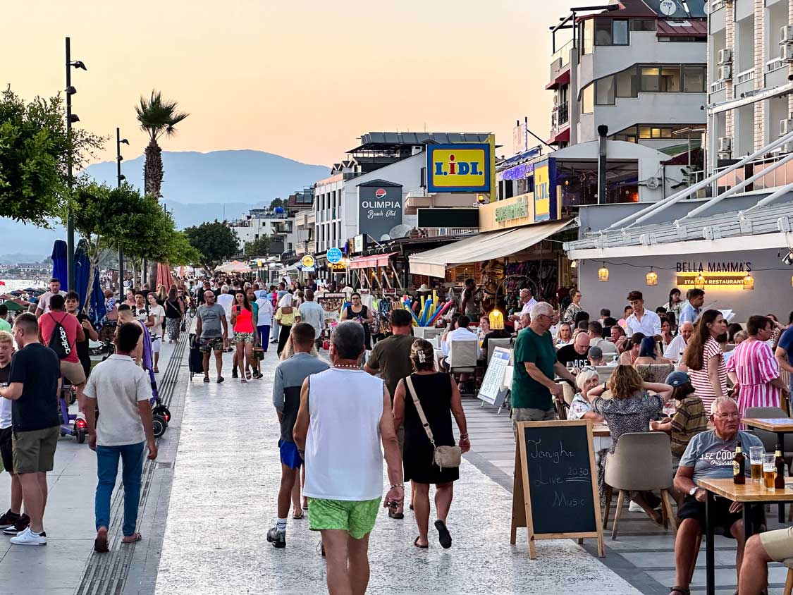 Crowds stroll down an oceanside boardwalk in Fethiye, Turkiye at sunset