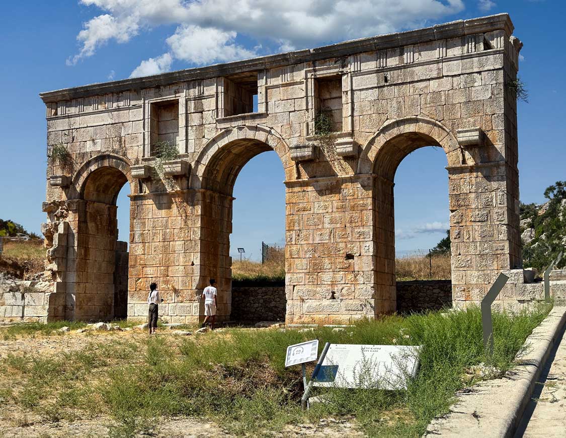 A large Lycian monument with three arched entrances sits in a field in Patara National Park