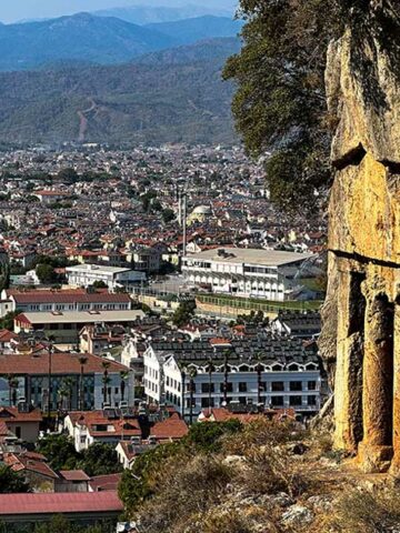 Things to do in Fethiye Turkiye image shows a Lycian rock tomb over a large Turkish city