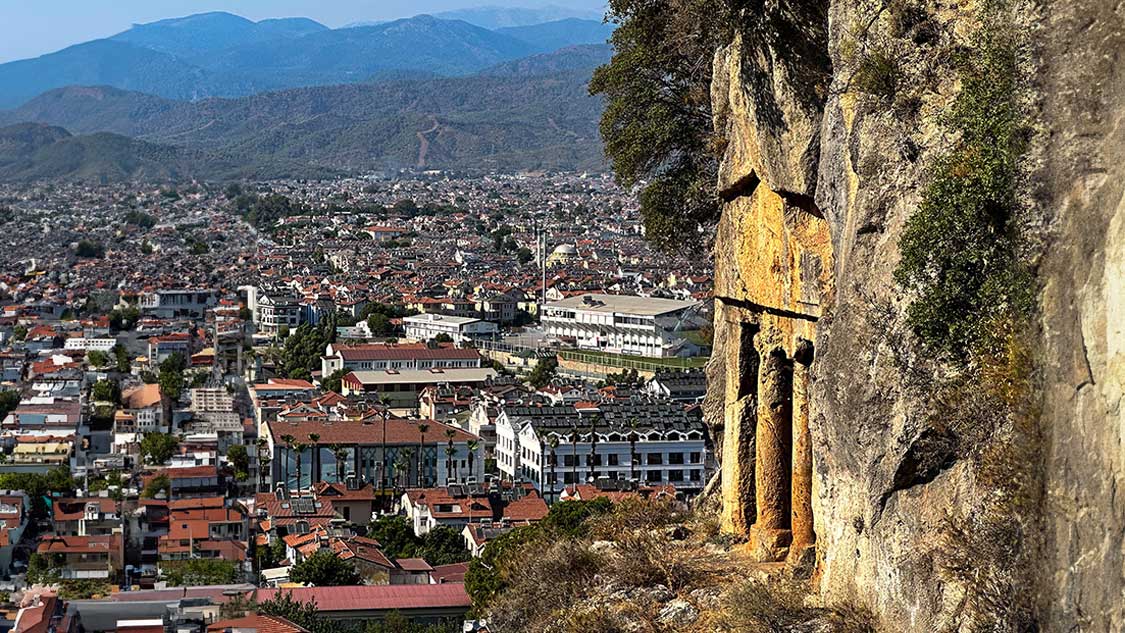 Things to do in Fethiye Turkiye image shows a Lycian rock tomb over a large Turkish city