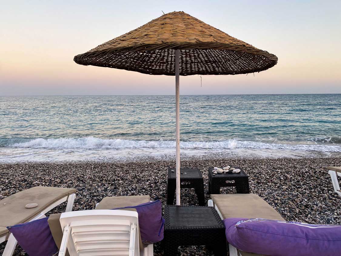 A straw umbrella and lounge chairs on Beymelek Beach in Demre