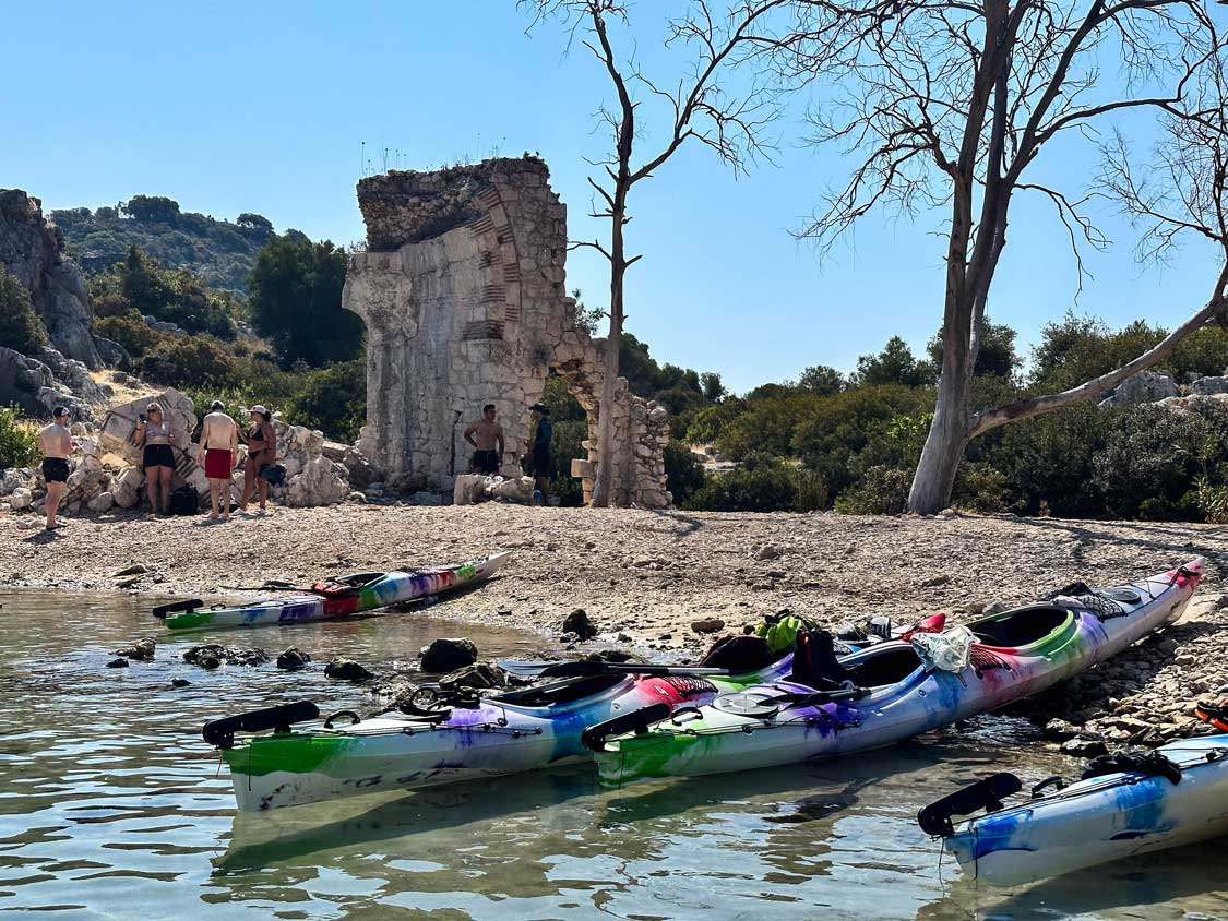 Kayaks line the shore in front of the remains of a Triumphal Arch on Kekova Island