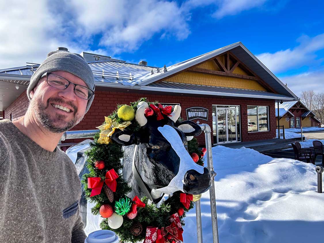A man poses with a cow statue at Fromagerie Montebello Quebec