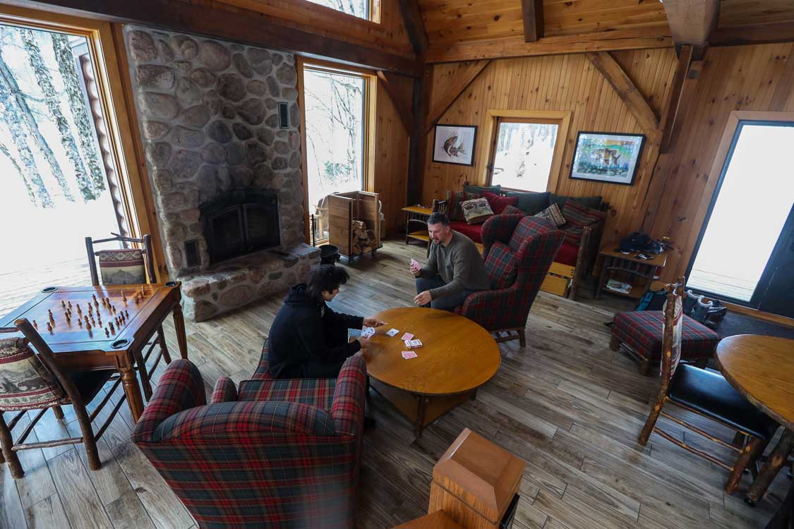 A father and son play cards in a cozy cabin at Kenauk Nature