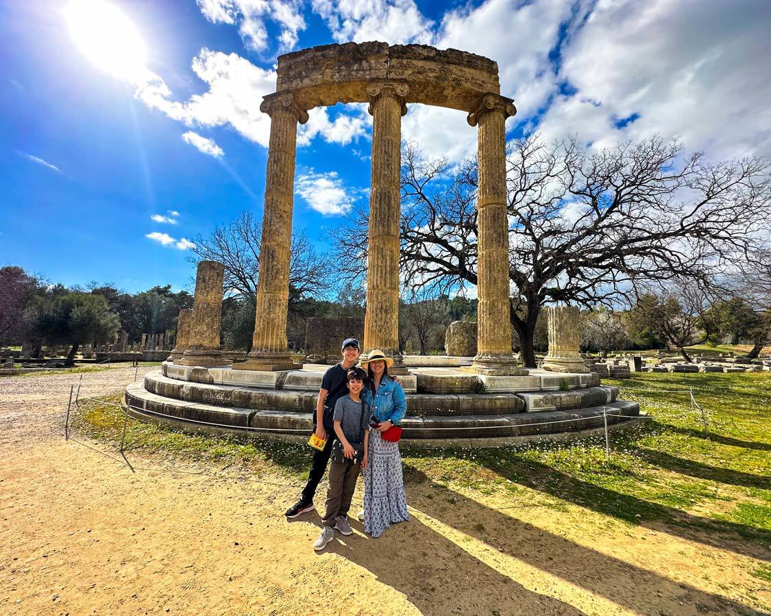 A mother and her kids walk past a temple in Olympia, Greece