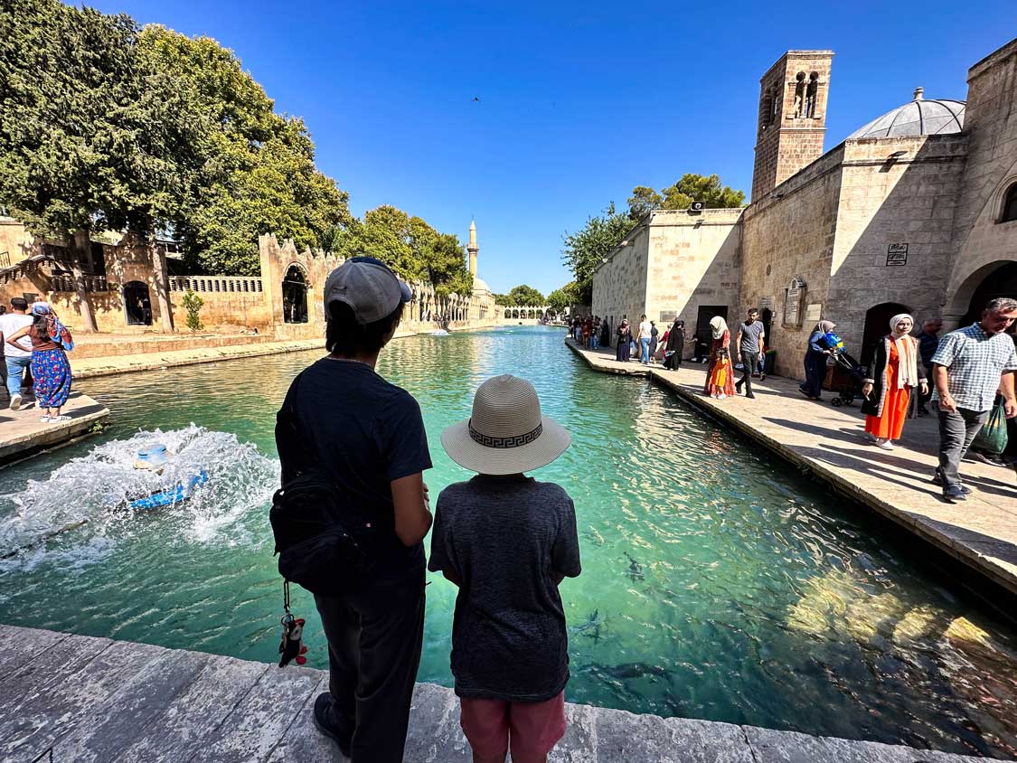 Two boys wearing hats look out over the Sacred pool in Sanliurfa, Turkiye