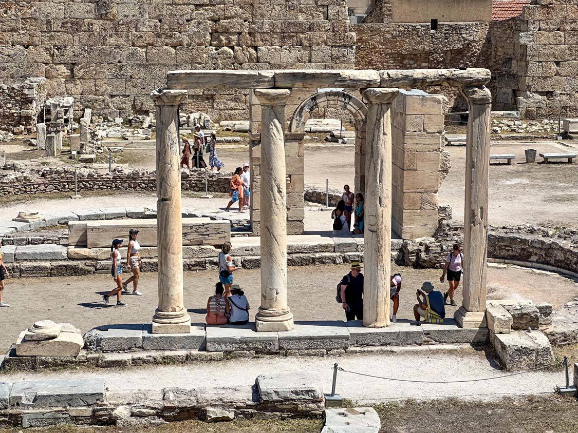 Crowds walk past a row of columns in the Ancient Agora in the Athens Plaka