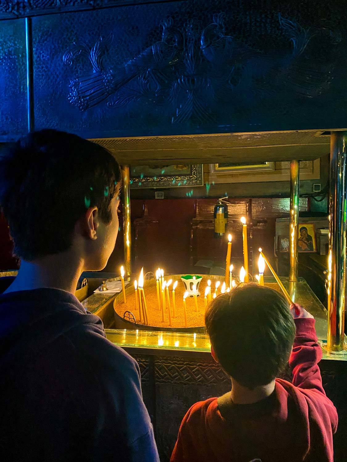 Two boys light candles at Saint Spyridon Church