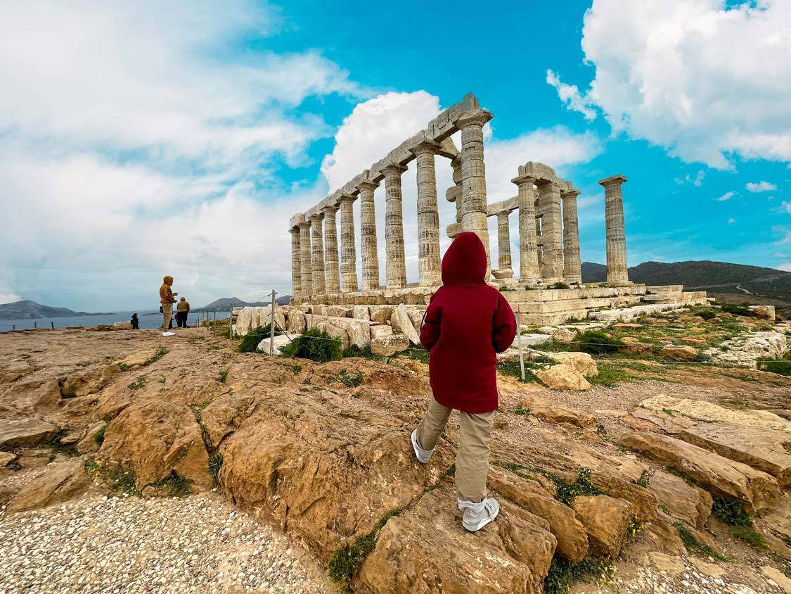 A young boy in a sweater walks toward the Temple of Poseidon