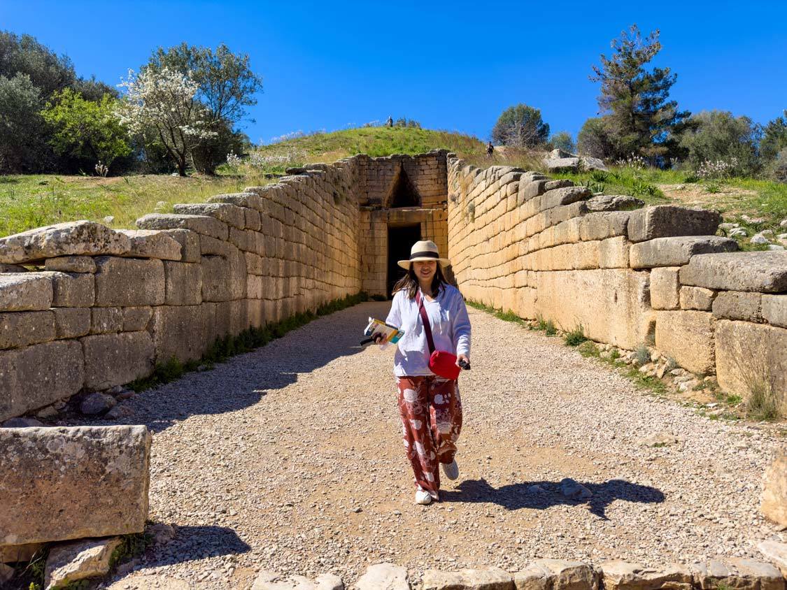 A woman holding a travel guide walks out of the Tomb of Clytemnestra in Mycenae