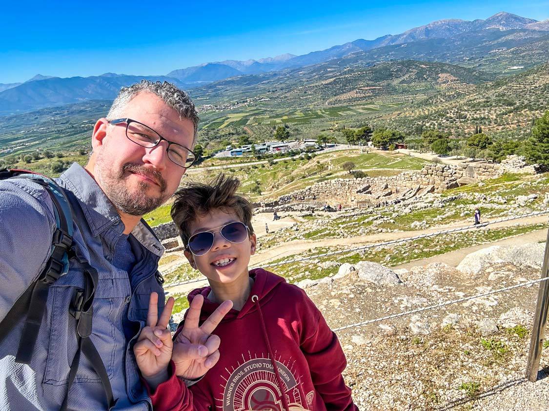 A father and son smile for the camera while exploring the Mycenae ruins