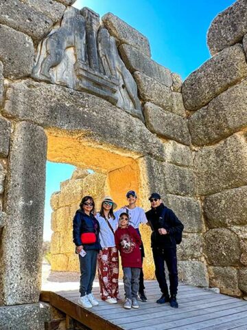 A multi-generational travel family poses in front of the Mycenae Lion Gate in Greece