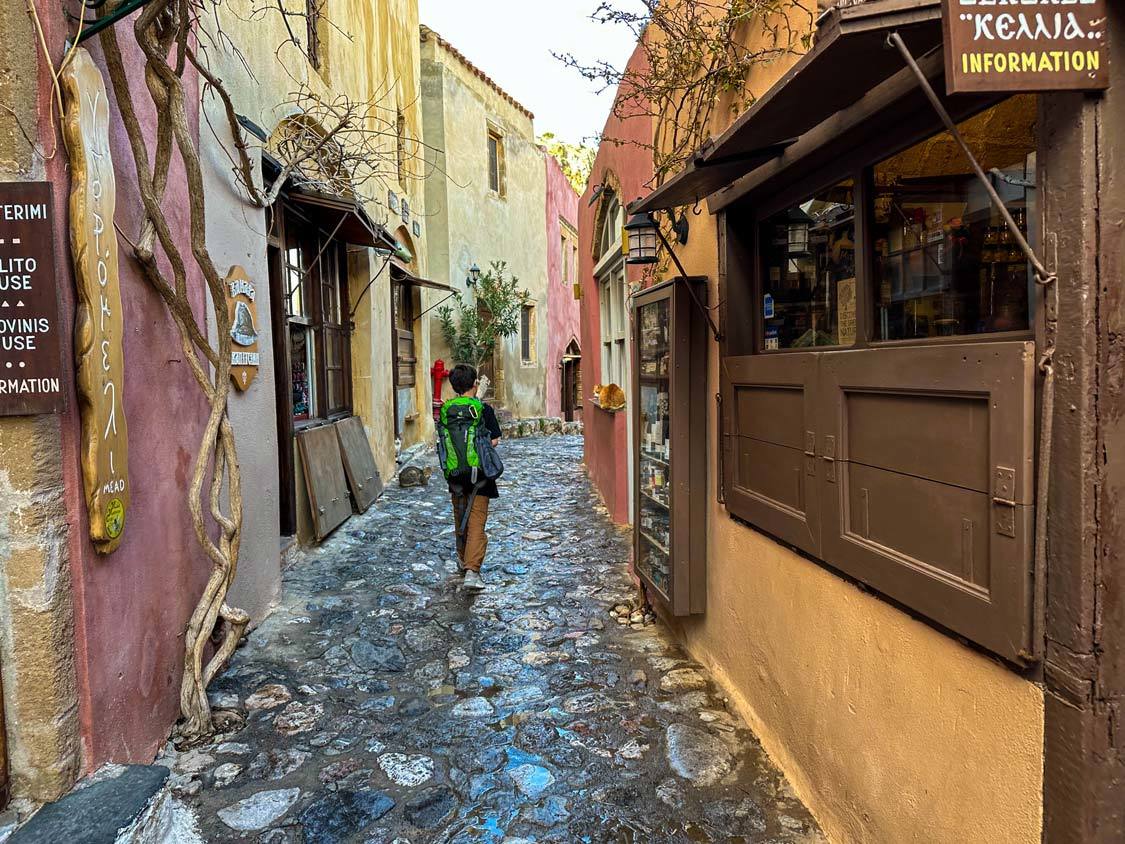 A boy with a green backpack walks through the narrow streets of Monemvasia, Greece