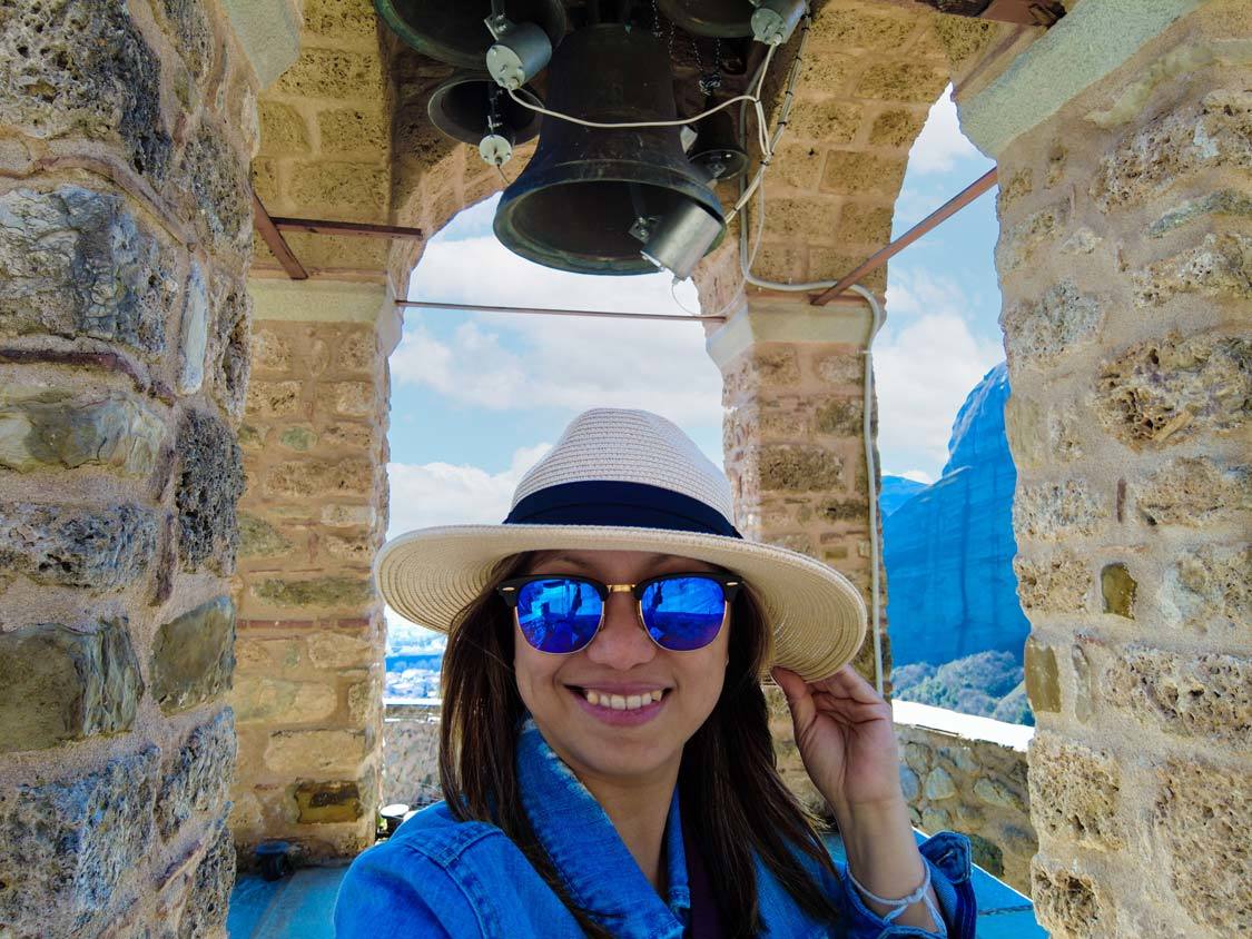 A woman holding her hat poses at the bell tower in the Monastery of Saint Nicholas