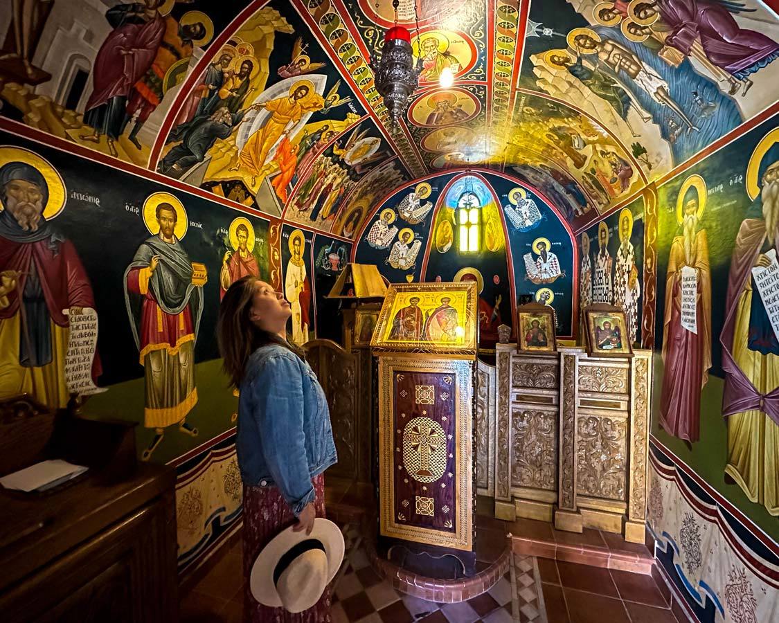 A woman in a small chapel looks up at frescoes on the ceiling