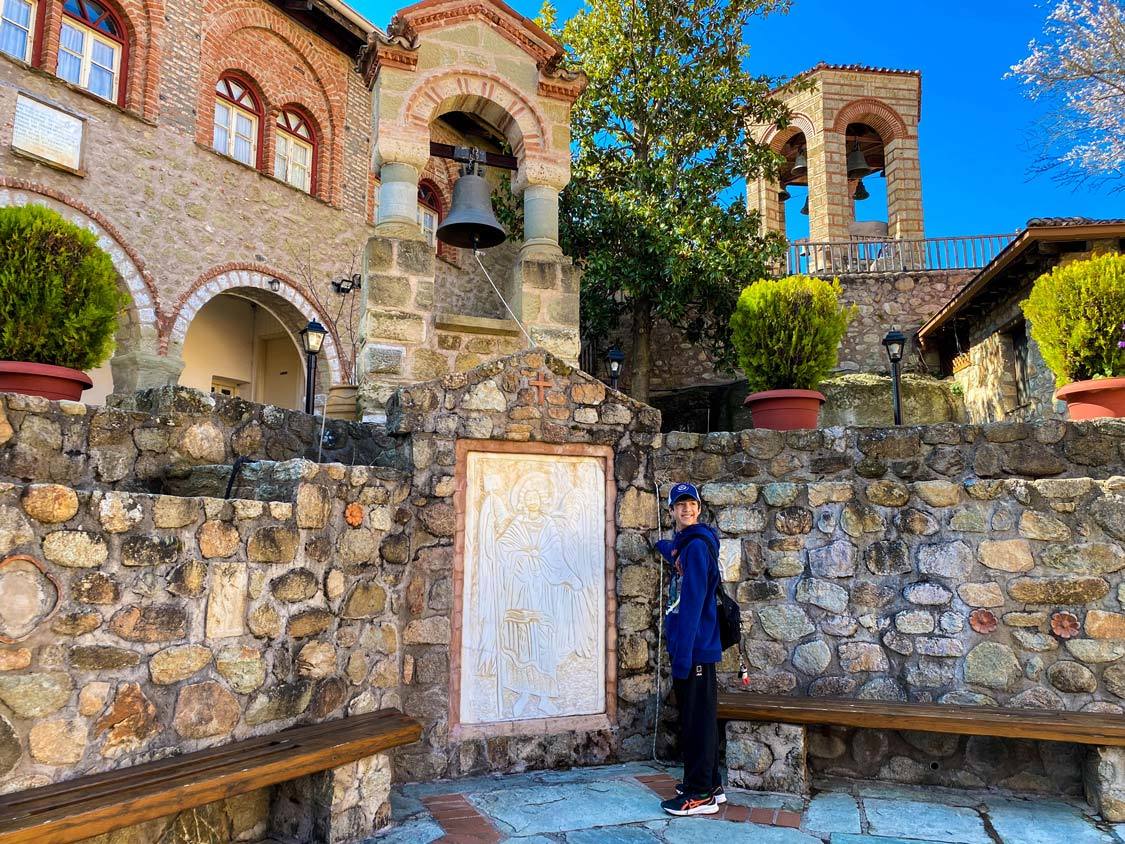 A teen boy poses with a carving of a saint at the Grand Meteoron Monastery