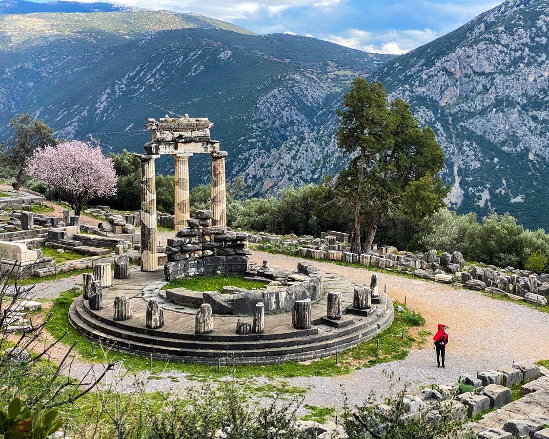 A boy in a red jacket waves to his family from the Temple of Athena in Delphi, Greece