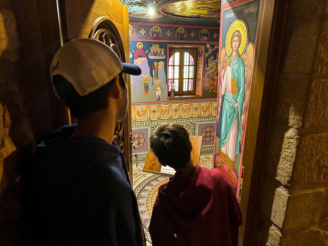 Two boys peek through a doorway into a colorfully painted room at the Roussano Nunnery in Meteora