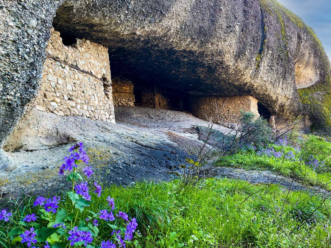 A hermit cave surrounded by wildflowers in Meteora, Greece