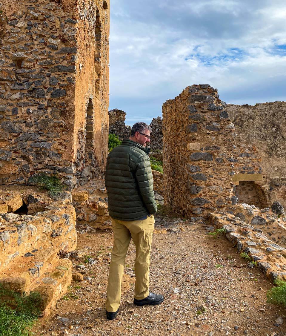 A man in travel gear walks by a church in the Monemvasia Acropolis