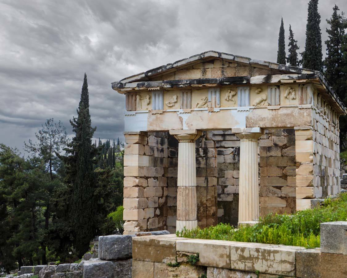 A stone building against a grey sky background with tall evergreen trees