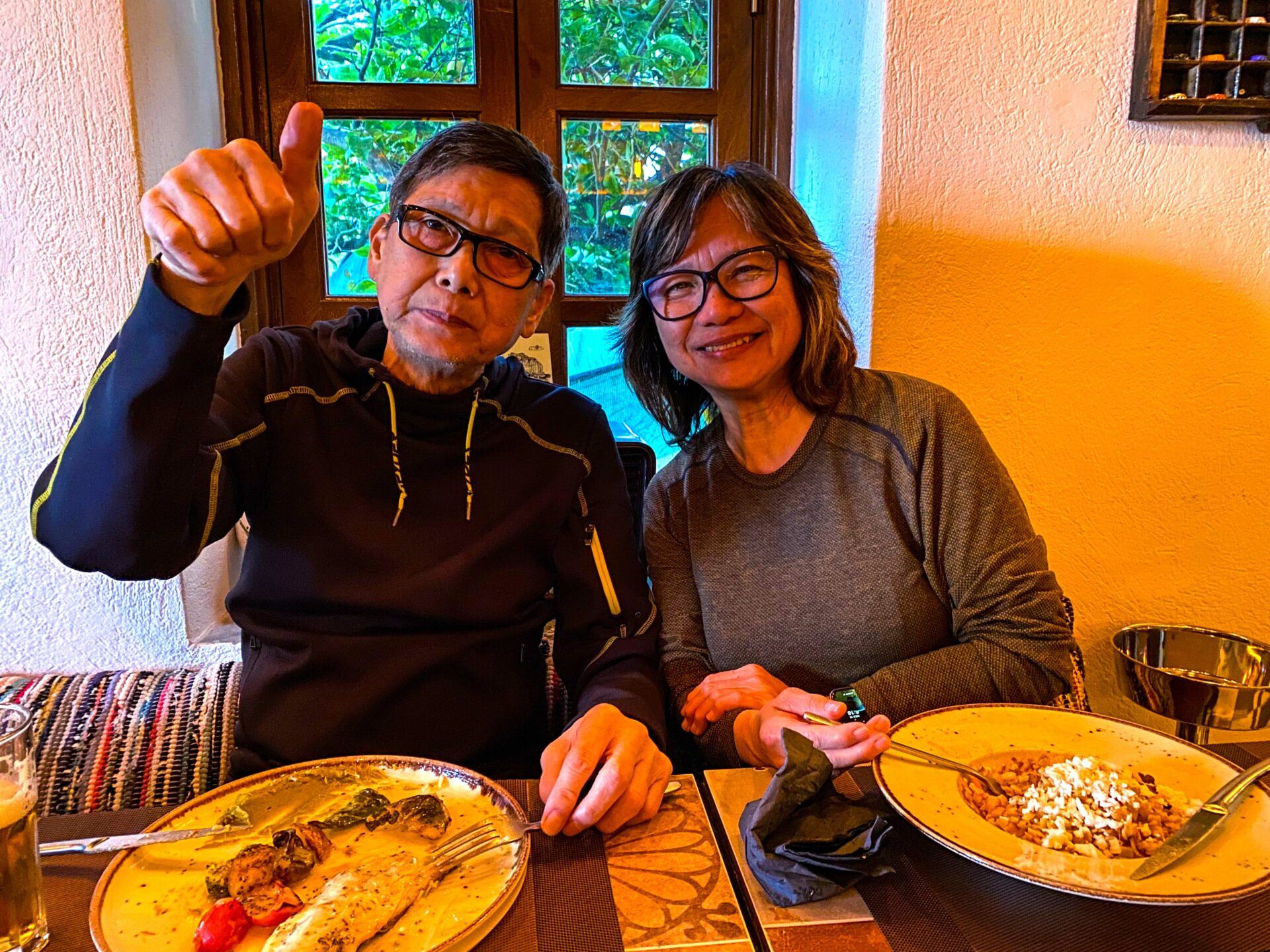 A middle-aged Filipino couple smiles while eating Greek food at Oinomelo Restaurant in Monemvasia, Greece