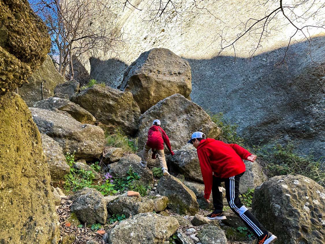 Two boys scramble over boulders on the Rock of the Great Saint Hike in Meteora