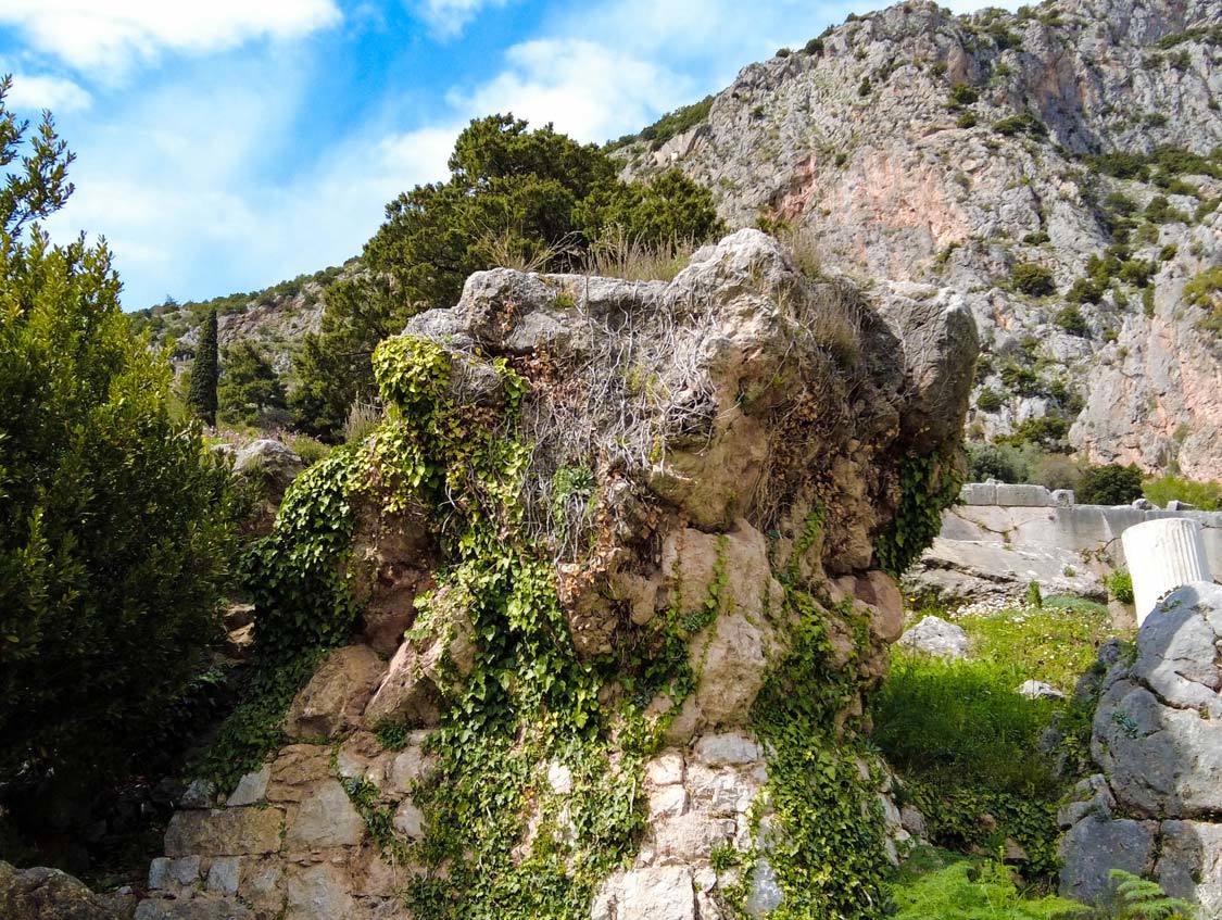 A large rock covered in moss and grass is the Pulpit of Pythia in Delphi