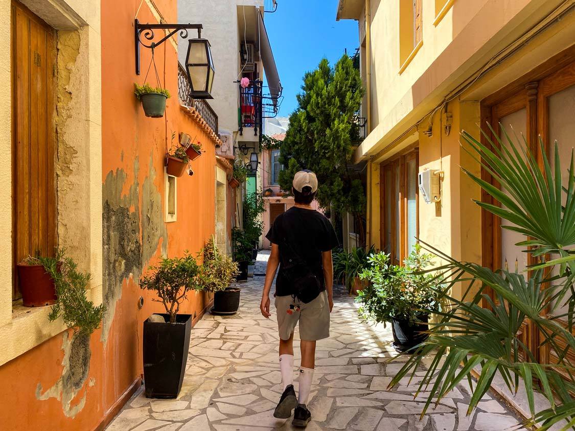 A young teen walks through a narrow alley lined with colorful houses in Archanes, Crete