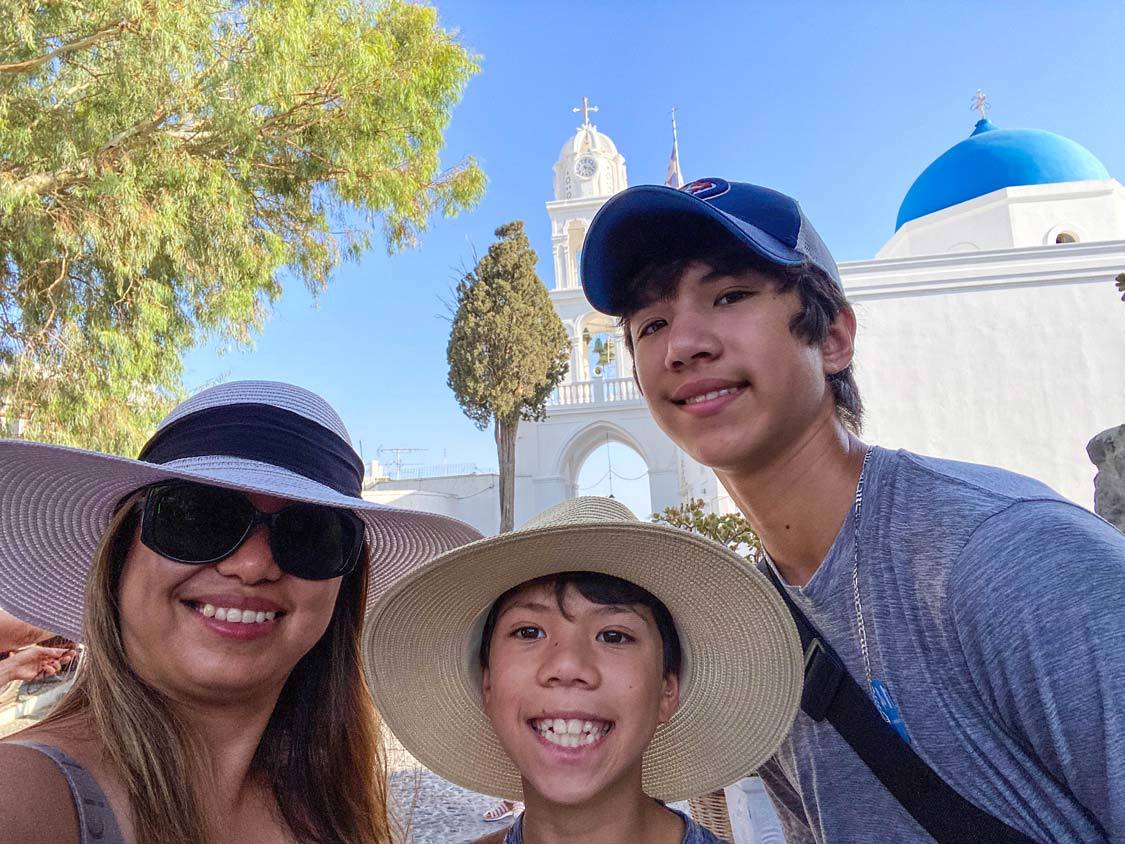 A mother and her two children smile in front of the Megalochorie Bell Tower