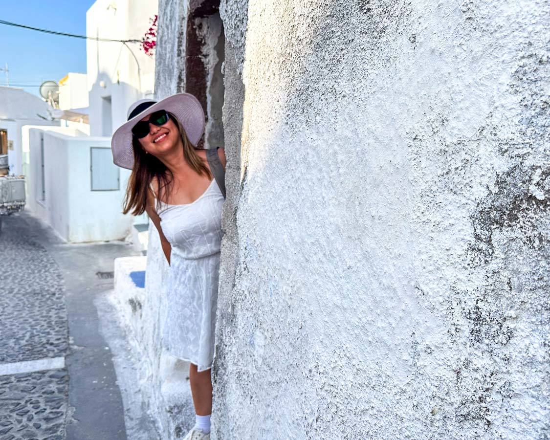 A Filipino woman in a white outfit smiles as she looks out from a shop in Megalochorie, Santorini