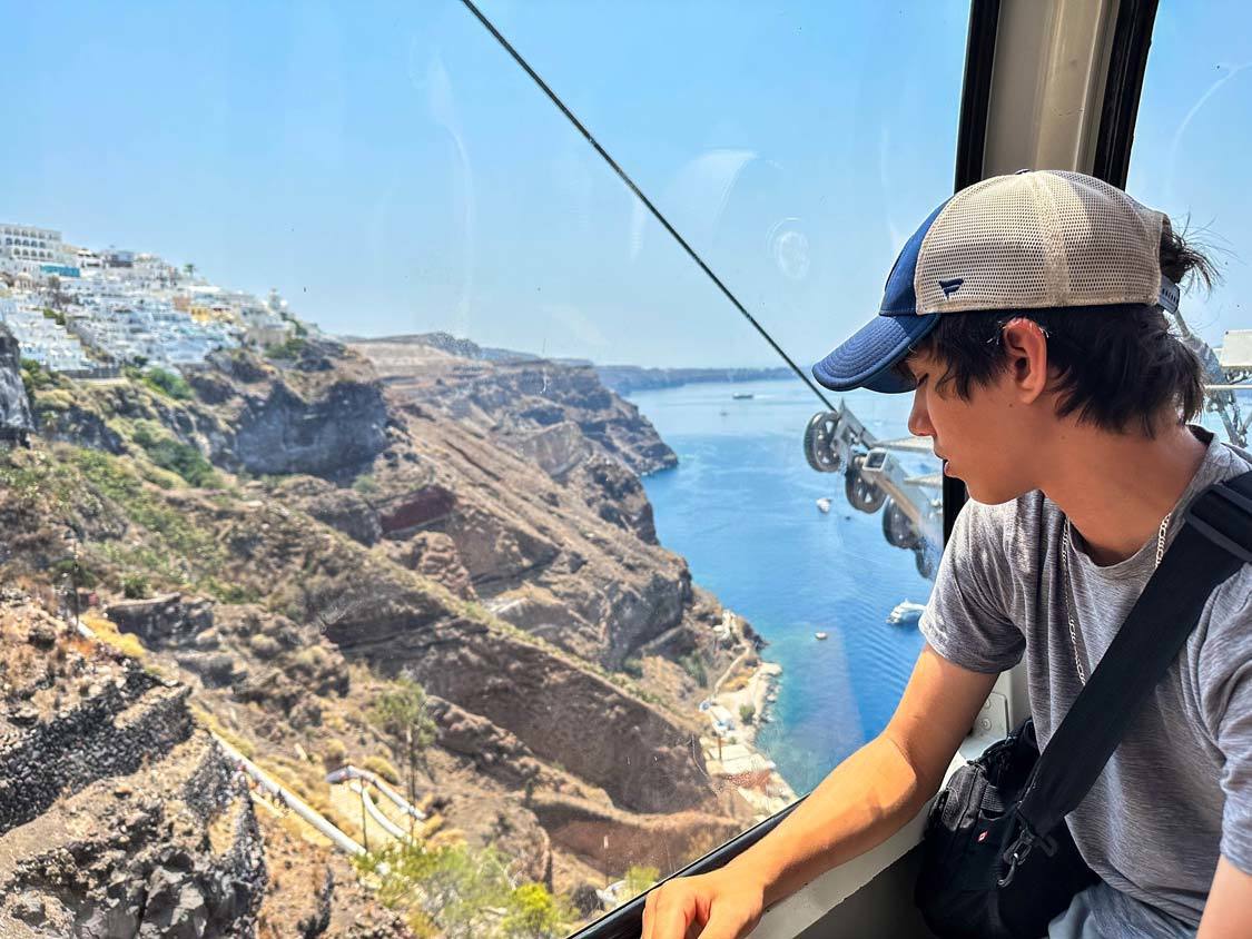 A young teen looks down over Santorini from a cable car