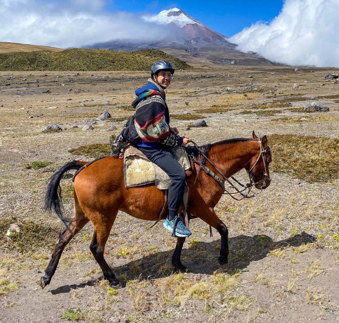 A teen rides a horse past Cotopaxi Mountain in Cotopaxi National Park