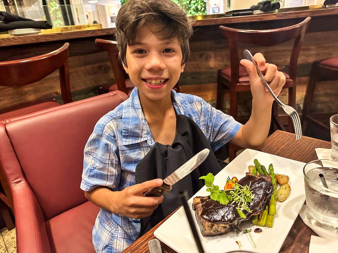 A smiling boy enjoys a steak and Asparagus at Elm Street Bar and Lounge in the Chlsea Hotel