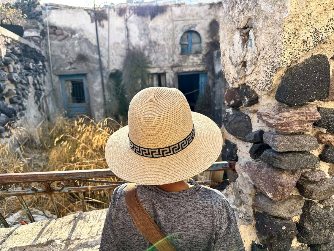 A young boy wearing a hat looks at a house destroyed by the 1956 Santorini Earthquake