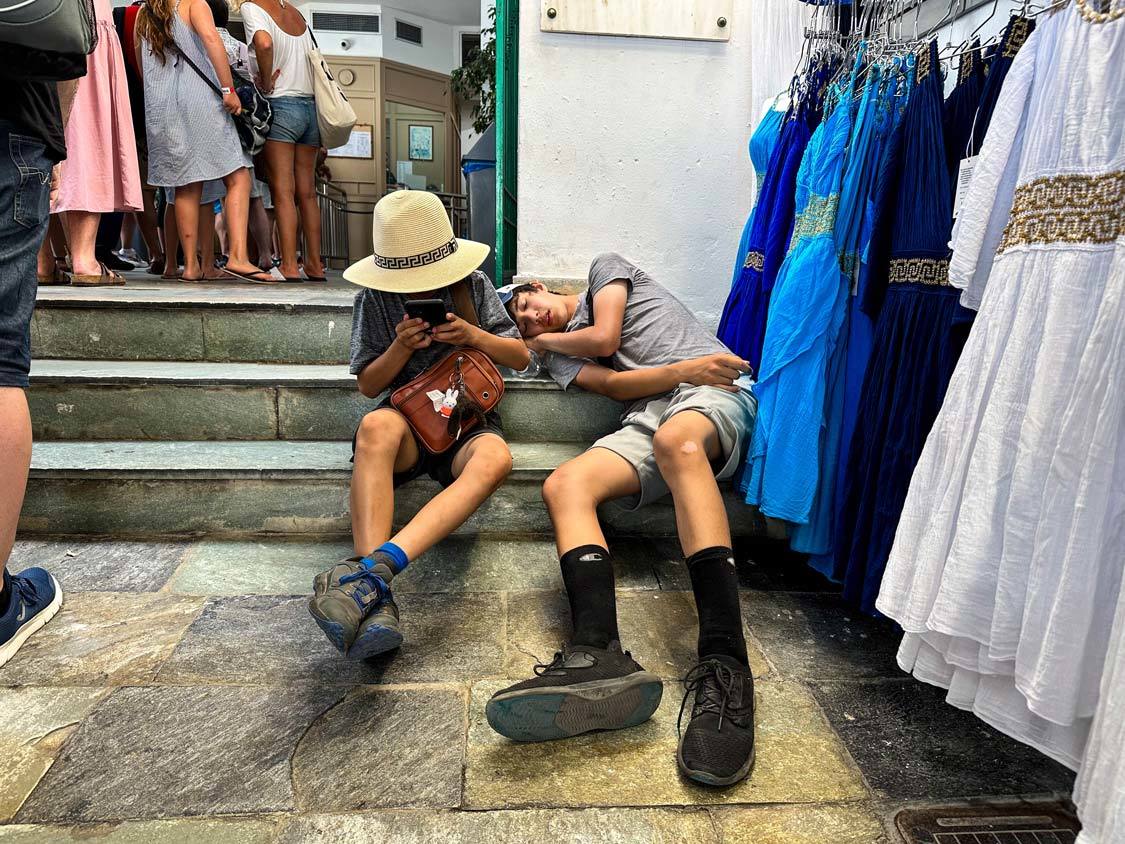 A young boy texts on his phone while sitting next to his sick  older brother in a stairwell in Oia, Santorini