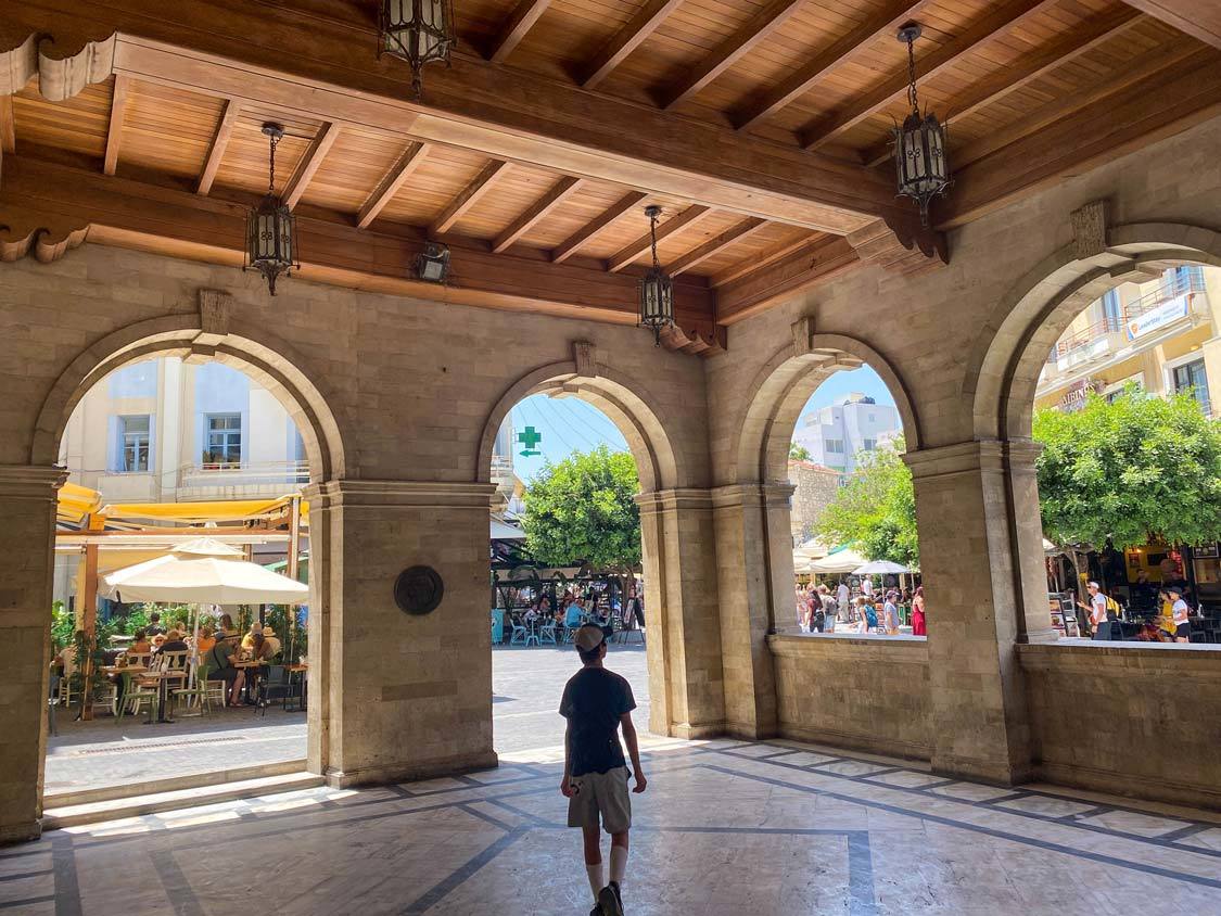 A young teen walks through the elegant archways of the Venetian Loggia in Heraklion, Greece