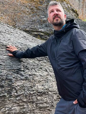 Man wearing a travel jacket while leaning against a rock