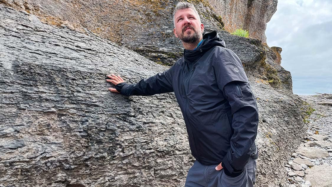 Man wearing a travel jacket while leaning against a rock