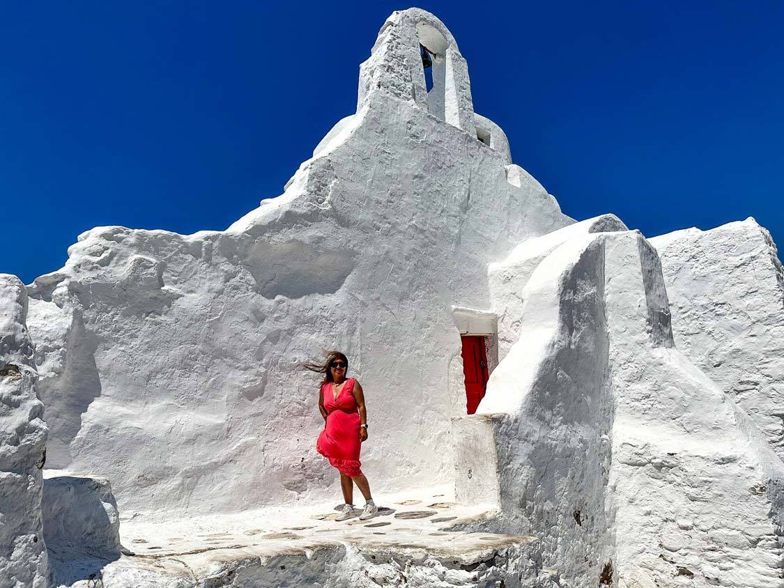 A woman in a pink dress climbs to the door of Panagia Paraportiani Church in Mykonos