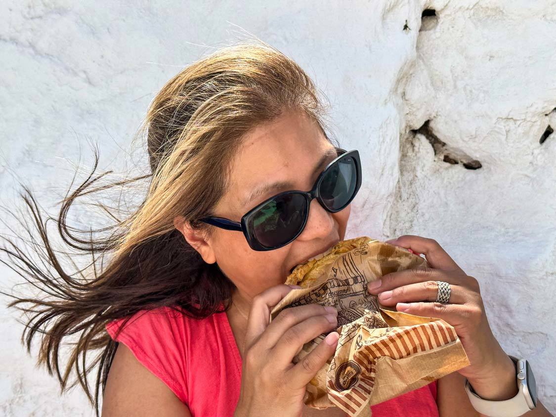 A woman eats a large sandwich in the sun of Chora, Mykonos