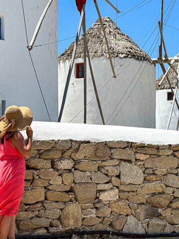 A woman in a pink dress looks at windmills during one day on Mykonos