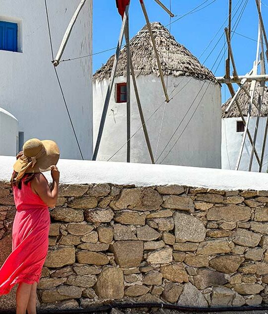 A woman in a pink dress looks at windmills during one day on Mykonos